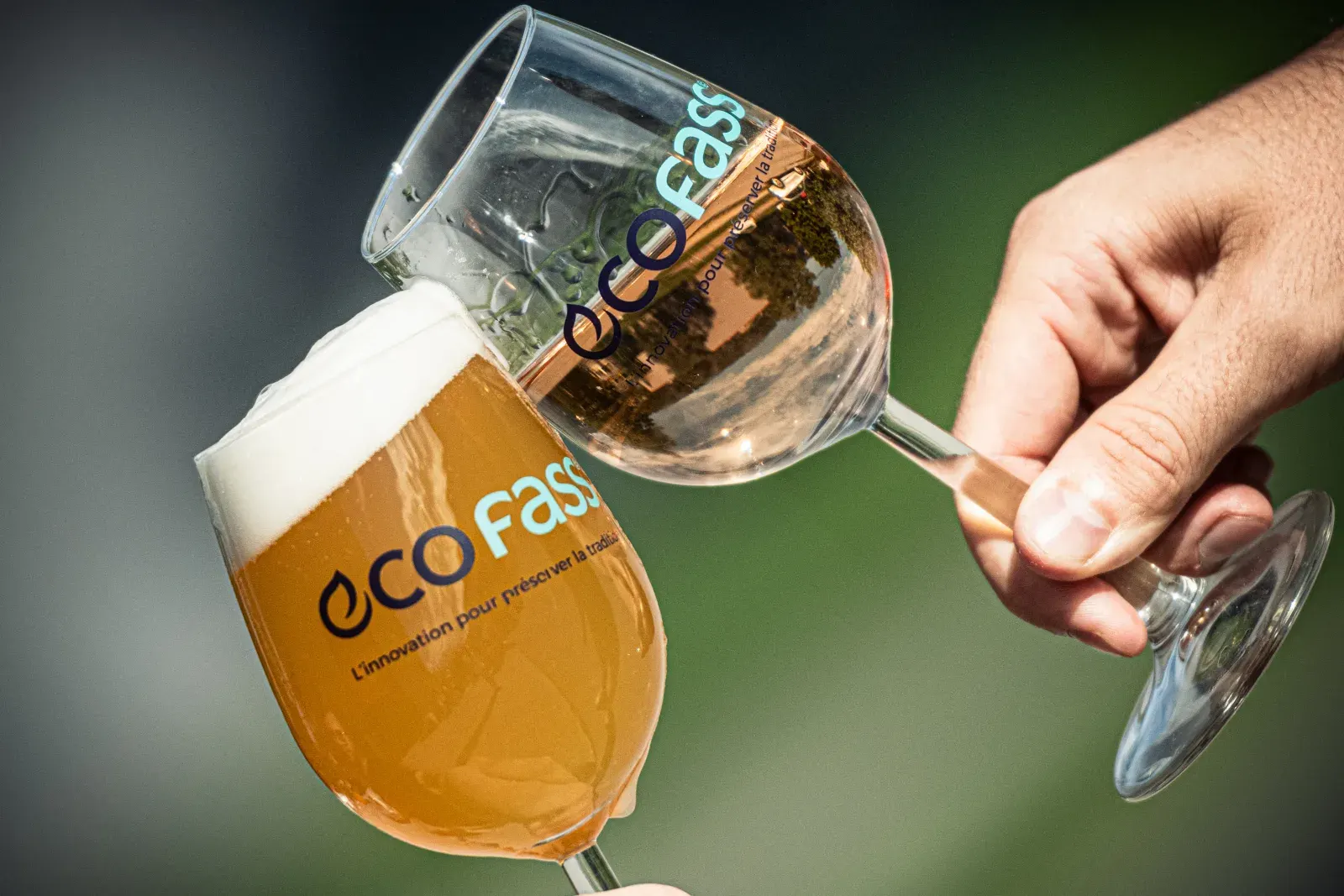 Deux verres ECOFASS trinquent en extérieur, l'un de bière ambrée, l'autre de rosé